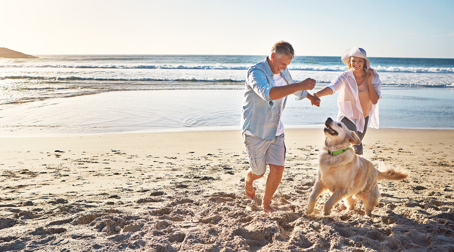a couple on the beach laughing playing with a dog